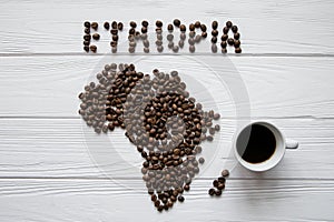 Map of the Ethiopia made of roasted coffee beans laying on white wooden textured background with coffee cup