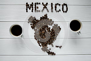 Map of the Mexico made of roasted coffee beans laying on white wooden textured background with two cups of coffee
