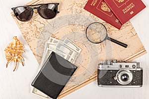 map, two passports, a magnifying glass, money in a black leather wallet, an old film camera, sunglasses and a shell on a white wo