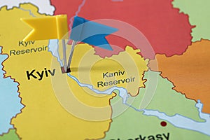 Map of Ukraine with blue and yellow flag push pins placed on Kyiv, closeup