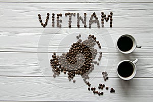 Map of the Vietnam made of roasted coffee beans laying on white wooden textured background with two cups of coffee
