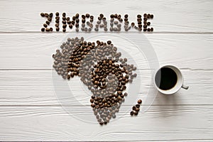 Map of the Zimbabwe made of roasted coffee beans laying on white wooden textured background with coffee maker with cup of cof