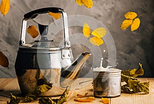 Maple leaves and hot tea in a tea set create an autumn mood. Falling leaves and splash of milk tea. Cozy
