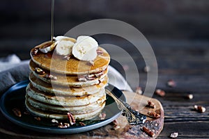 Maple syrup pouring onto pancakes against dark background