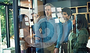 Mapping out an approach to reaching their goals. a group of businesspeople brainstorming with notes on a glass wall in