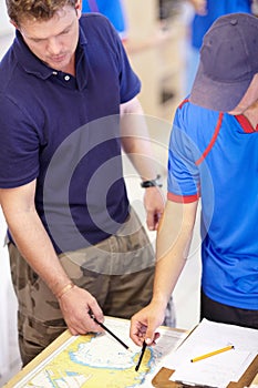 Mapping out the location. Cropped shot of two male lifeguards finding co-ordinates on a map in their office.