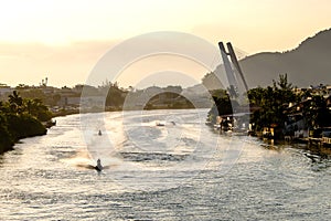 Marapendi Lagoon seen from above with houses on the hill during sunset, golden light. Jet skis are riding on the lake. Barra da Ti