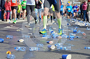 Marathon running race, runners feet and plastic water cups on road near refreshment point, sport