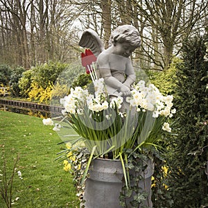 The Marble angel in front of a vase with daffodils in a botanical garden