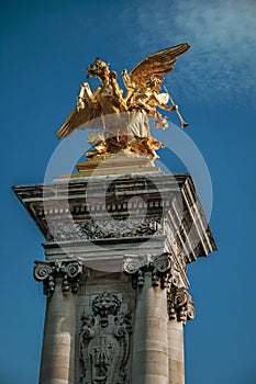 Marble column with golden statue adorning the Alexandre III bridge over the Seine River in Paris.