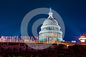 Marble dome of the United States Capitol building illuminated by rays of architectural light on a clear blue night with fountain