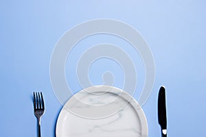 Marble empty plate with fork and knife over the blue background.