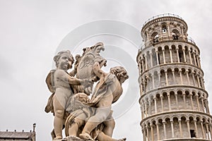 The marble Fountain of Angels Fontana dei Putti in front of The Leaning Tower of Pisa.  Tuscany, Italy