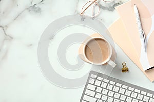 Marble office desk table with office supplies, coffee cup, eye glasses, keyboard. Top view with copy space, flat lay