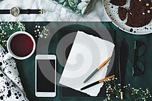 Marble pattern table with top view of empty paper with two quill pens, glasses, mug with tea and mockup phone