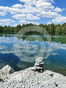 Marble pyramid on the shore of Lake Svetloye with turquoise water, which reflects the trees, and the sky with clouds, in the