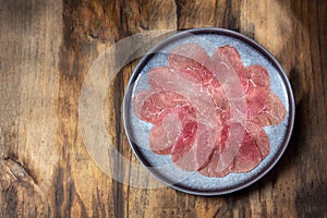 Marbled beef for carpaccio with ingredients arugula and capers on gray plate, wooden background, top view