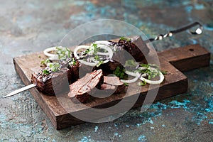 Marbled beef skewer with pickled onions and herbs on a wooden cutting board