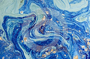 Marbled blue abstract background with golden sequins. Liquid marble ink pattern.