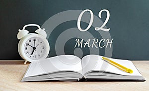 March 02. 02-th day of the month, calendar date. A white alarm clock, an open notebook with blank pages, and a yellow pencil lie