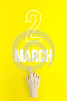 March 2nd. Day 2 of month, Calendar date.Hand finger pointing at a calendar date on yellow background.Spring month, day of the