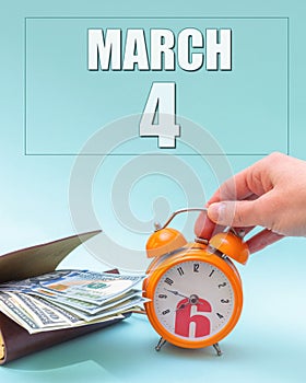 March 4th. Hand holding an orange alarm clock, a wallet with cash and a calendar date. Day 4 of month.