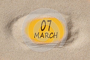 March 7. 7th day of the month, calendar date. Hole in sand. Yellow background is visible through hole
