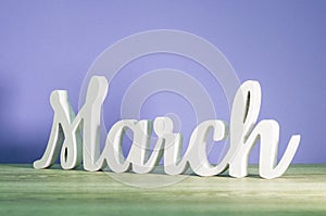 March - biginning of springtime concept. Wooden carved inscription on purple or dark pink background