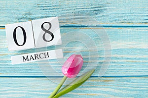 8 March date written on white cubes with pink tulip flower on bright blue wooden background with copy space