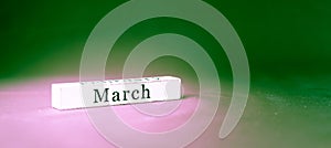 March, name of the month written on vintage white wooden block on green textured background . Banner format