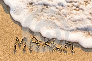 March - word drawn on the sand beach with the soft wave.