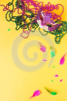 Mardi gras accessories flat lay on bright yellow background, top view, copy space. Frame with traditional Mardi gras beads, masks