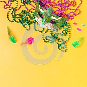 Mardi gras accessories flat lay on bright yellow background, top view, copy space. Frame with traditional Mardi gras beads, masks