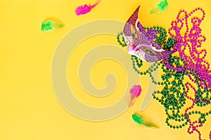 Mardi gras accessories flat lay on bright yellow background, top view, copy space. Frame with traditional Mardi gras beads, masks