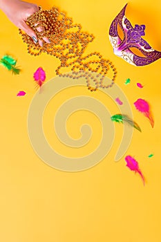 Mardi gras accessories flat lay on bright yellow background, top view, copy space. Frame with traditional Mardi gras beads, masks