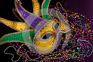 A Mardi gras jester's mask with beads on a black background