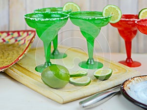 Margaritas in red and green glasses with salted rims and lime garnishes