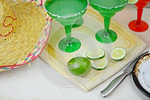 Margaritas in red and green glasses with salted rims and lime garnishes