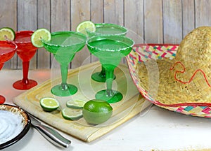 Margaritas in red and green glasses with salted rims and lime garnishes