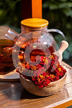 Marigold flower healthy tea in glass mug with tea pot on garden table. Herbal medicine Delicious tisane tea with fresh