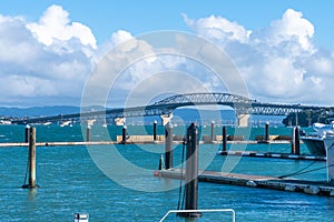 Marina piers and luxury boats form foreground from Stanley Bay for distant Auckland Harbour bridge