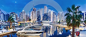 Marina with yachts and skyscrapers in Dubai UAE with Burj Khalifa at night.