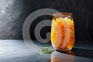 Marinated cabbage and carrots in a glass jar, with parsley, on dark kitchen countertop. Sauerkraut. Generative AI