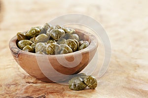 Marinated capers in bowl on olive board