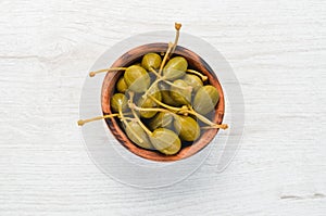 Marinated capers in a bowl on a white wooden background. Top view.