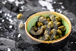 Marinated capers in a ceramic bowl. Edible flower buds of Capparis spinosa, caper bush or Flinders rose on a dark background