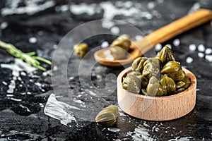 Marinated capers in a woden bowl. Edible flower buds of Capparis spinosa, caper bush or Flinders rose on a dark background