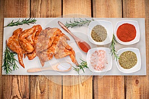 Marinated chicken wings raw.Chicken wings marinated in red sauce on a plate on a wooden background with different spices. Raw