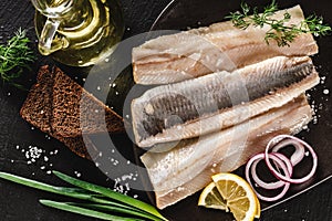 Marinated fillet mackerel or fillet herring fish with spices, greens and slice of bread on plate over dark stone background.