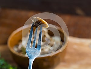 Marinated honey fungus in brown bowl on wooden table.